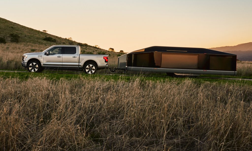 A silver truck towing a trailer in a field, showcasing the harmony of nature and transportation.