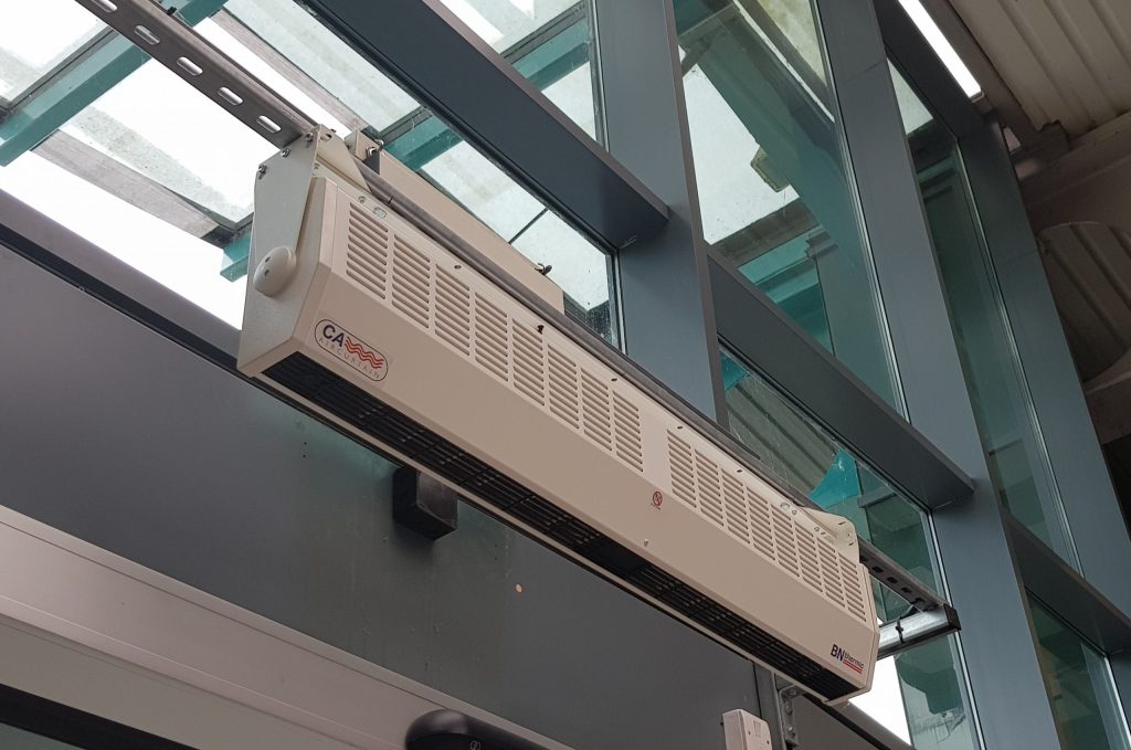 Photograph of a large grey overdoor air curtain above a shopping centre door. 